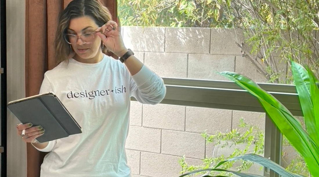 Woman holding an ipad wearing a white long sleeve t-shirt that says Designerish in black letters