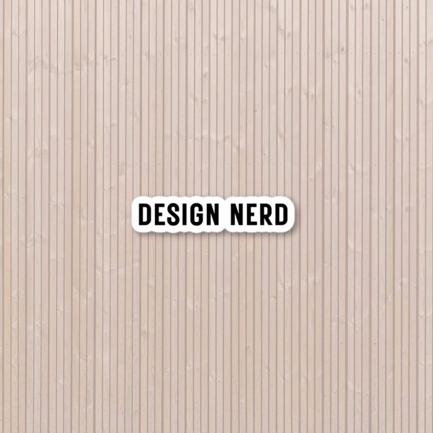 Wood slat background with white background sticker and in black block font says "Design Nerd"